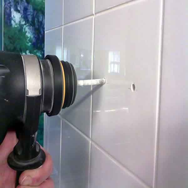 Image of someone with a large Drill resting on a Tiled Wall ready to Drill