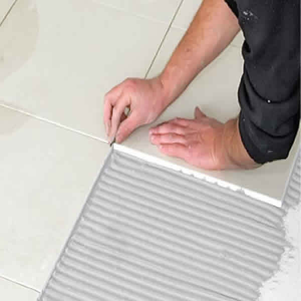 image of someone Tiling a Floor with mid range Beige tile, adheisive is on the floor ready for the Tile